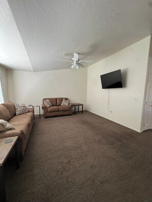 A living room with a brown sofa, a small table, a ceiling fan, and a mounted TV. - Quiet Home Near Everything (Hermiston)