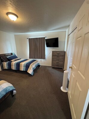 A bedroom with two beds, a television, a dresser, and a door. - Quiet Home Near Everything (Hermiston)