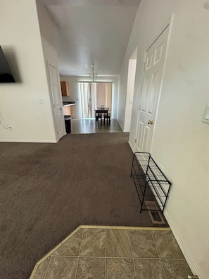 A hallway with carpet flooring, a tiled area at the end, and a dining area with a table and chairs.