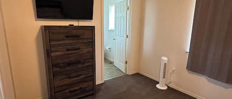 A bedroom with a bed, a dresser, a television mounted on the wall, and a door leading to another room.