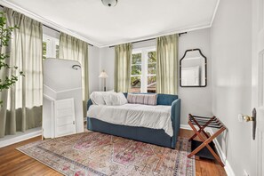 A bedroom with a bed, a window, a mirror, and a hanging plant.