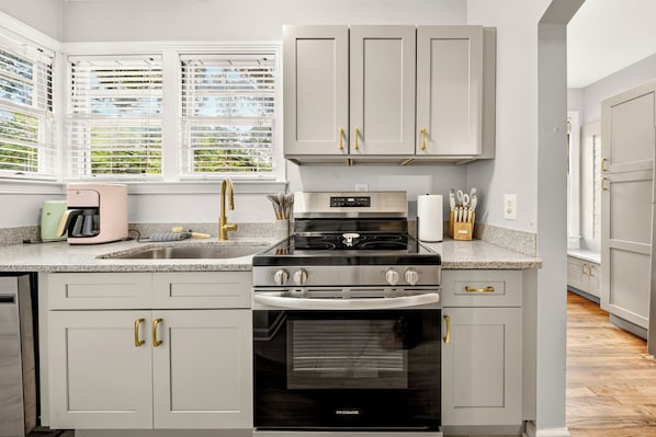 A kitchen with a gas stove, oven, and a window with blinds.