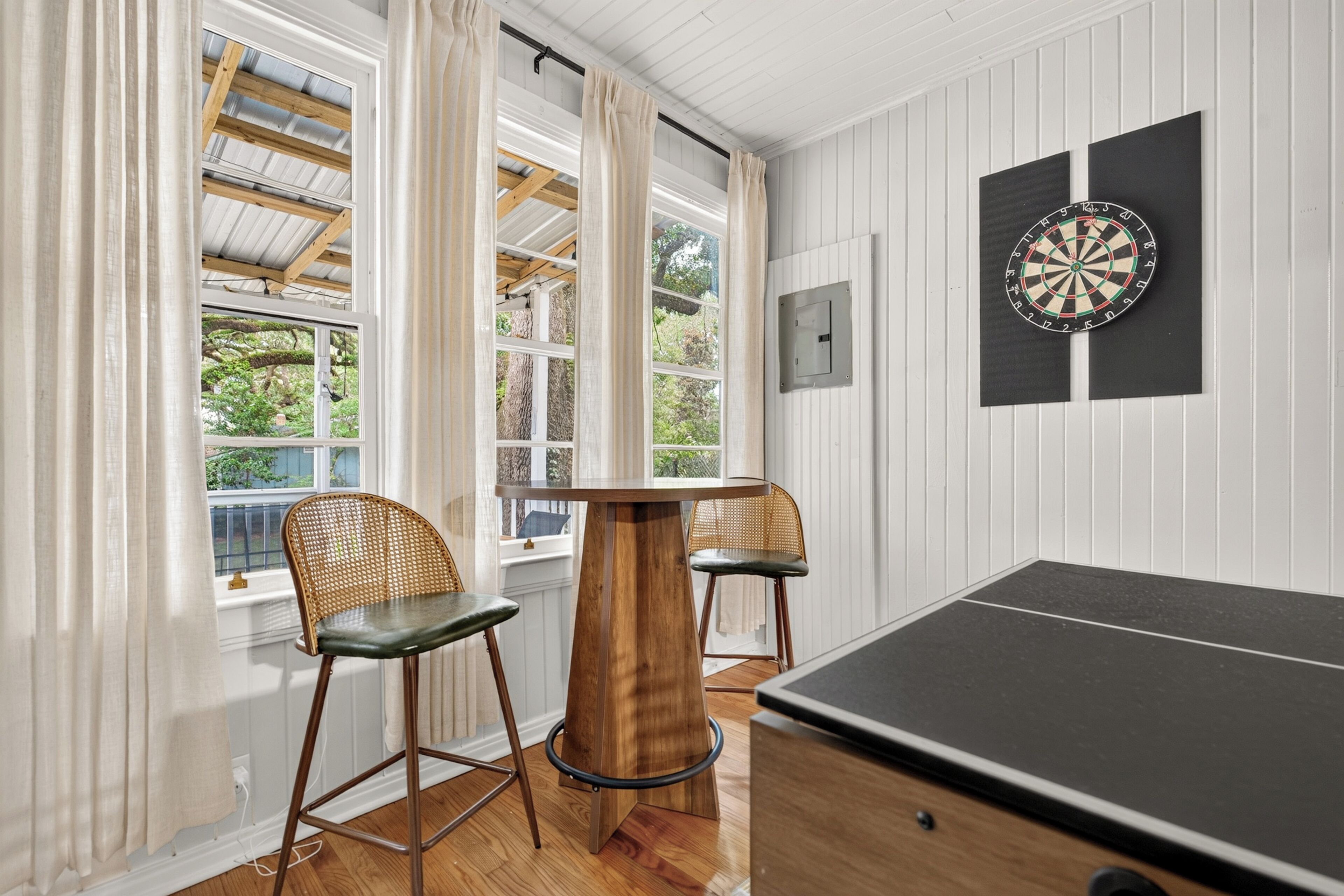 A room with a dartboard, two bar stools, and a pool table.