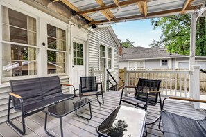 A covered porch with a glass table and two chairs, a wooden bench, and a white fence in the background. - Midtown - Backyard + Game Room + Deck + 2 Car Garage (Mobile)
