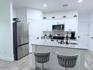 Eine moderne Küche mit weißen Schränken, Edelstahlgeräten, Granit Arbeitsplatten und zwei Barhocker.