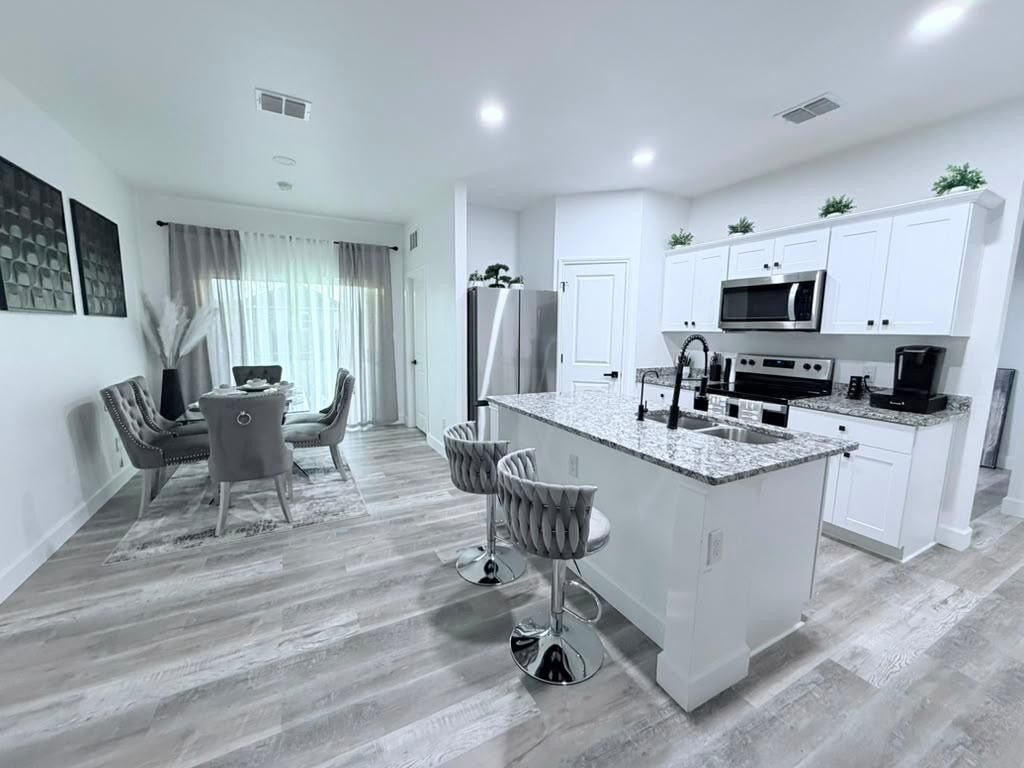 Une cuisine moderne avec des meubles blancs, un îlot central doté d’un comptoir en granit et des appareils électroménagers en acier inoxydable.