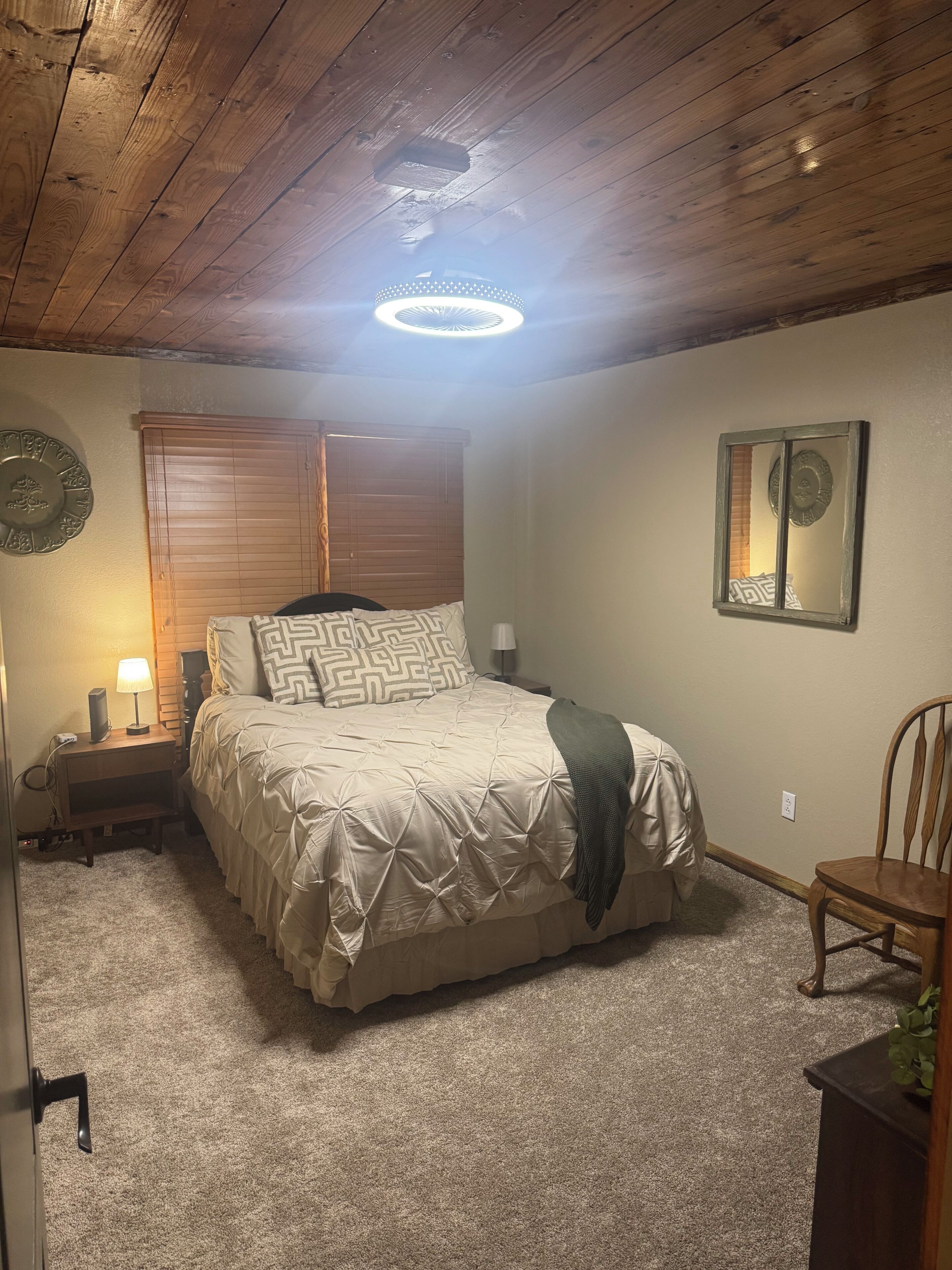 A bedroom with a bed, a nightstand, a lamp, a wall clock, and a ceiling light.