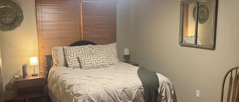 A bedroom with a bed, a nightstand, a lamp, a wall clock, and a ceiling light.
