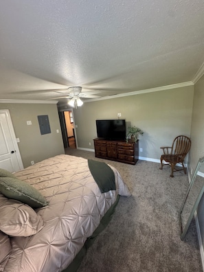 Un dormitorio con cama, cómoda, televisor y una silla.