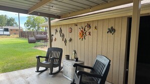 Un patio cubierto con dos mecedoras, una mesa y decoración en la pared.
