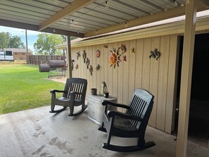A covered patio area with two rocking chairs, a table, and decorative wall art.
