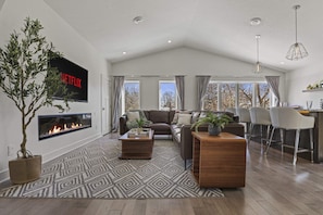 A modern living room with a fireplace, a flat-screen TV, a sofa, a coffee table, and a dining area with chairs. - 10min to US Bank Stadium & U of M w/ Fireplace (Minneapolis)