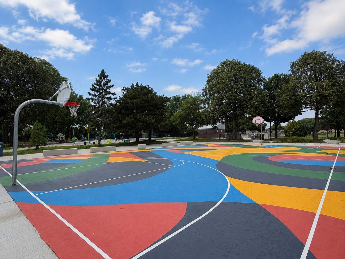 En utomhusbasketplan med en färgstark design, omgiven av träd och en klar himmel.