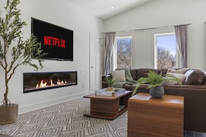 Una sala de estar moderna con chimenea, un televisor de pantalla plana grande montado en la pared, un sofá de cuero marrón y una mesa de centro.
