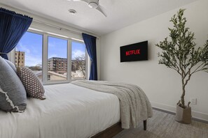 A bedroom with a bed, a large window, a wall-mounted TV, and a potted plant. - 10min to US Bank Stadium & U of M w/ Fireplace (Minneapolis)