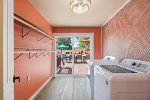 A laundry room with a washing machine, a drying rack, and a view of an outdoor patio area.
