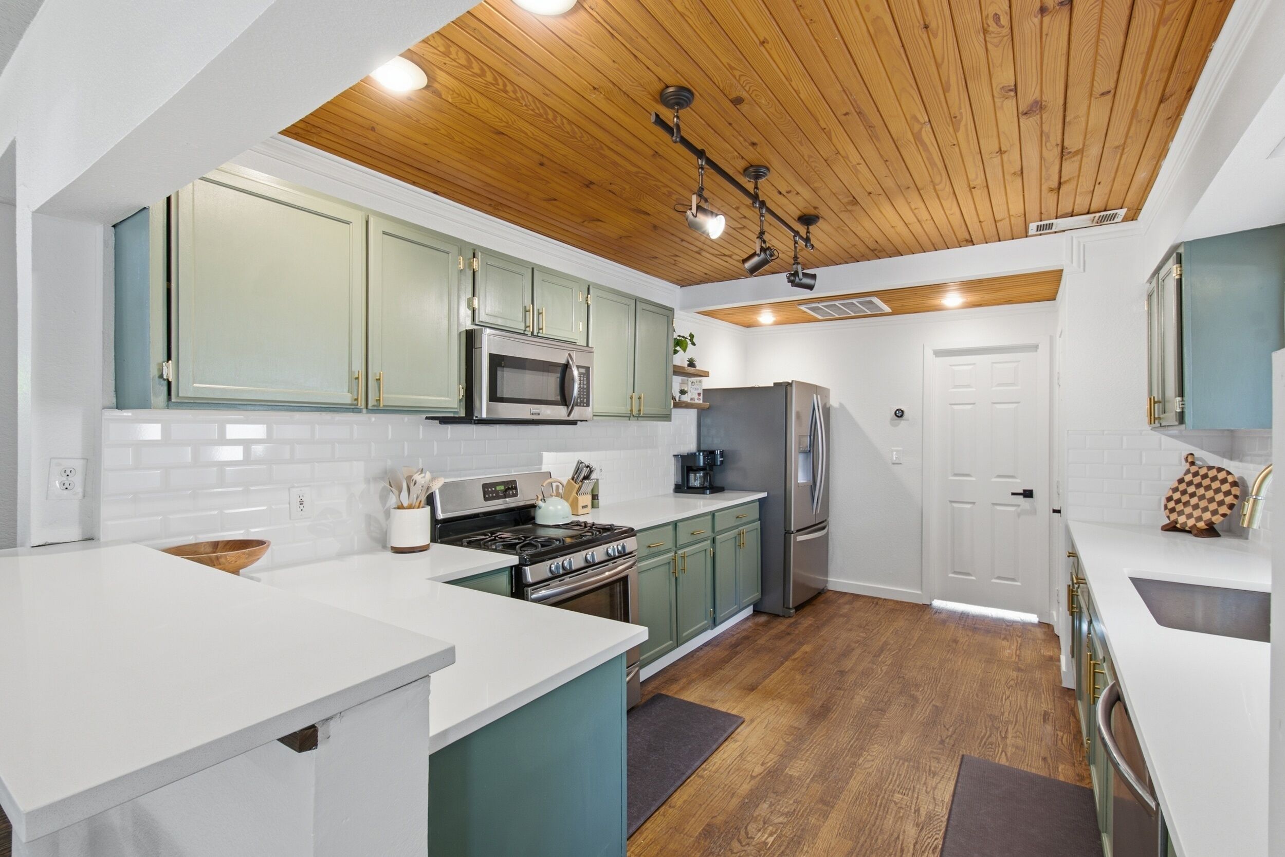 A modern kitchen with a central island, wooden ceiling, and built-in appliances.