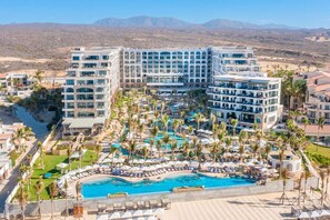 Un hotel con diversi edifici, una piscina centrale e palme.