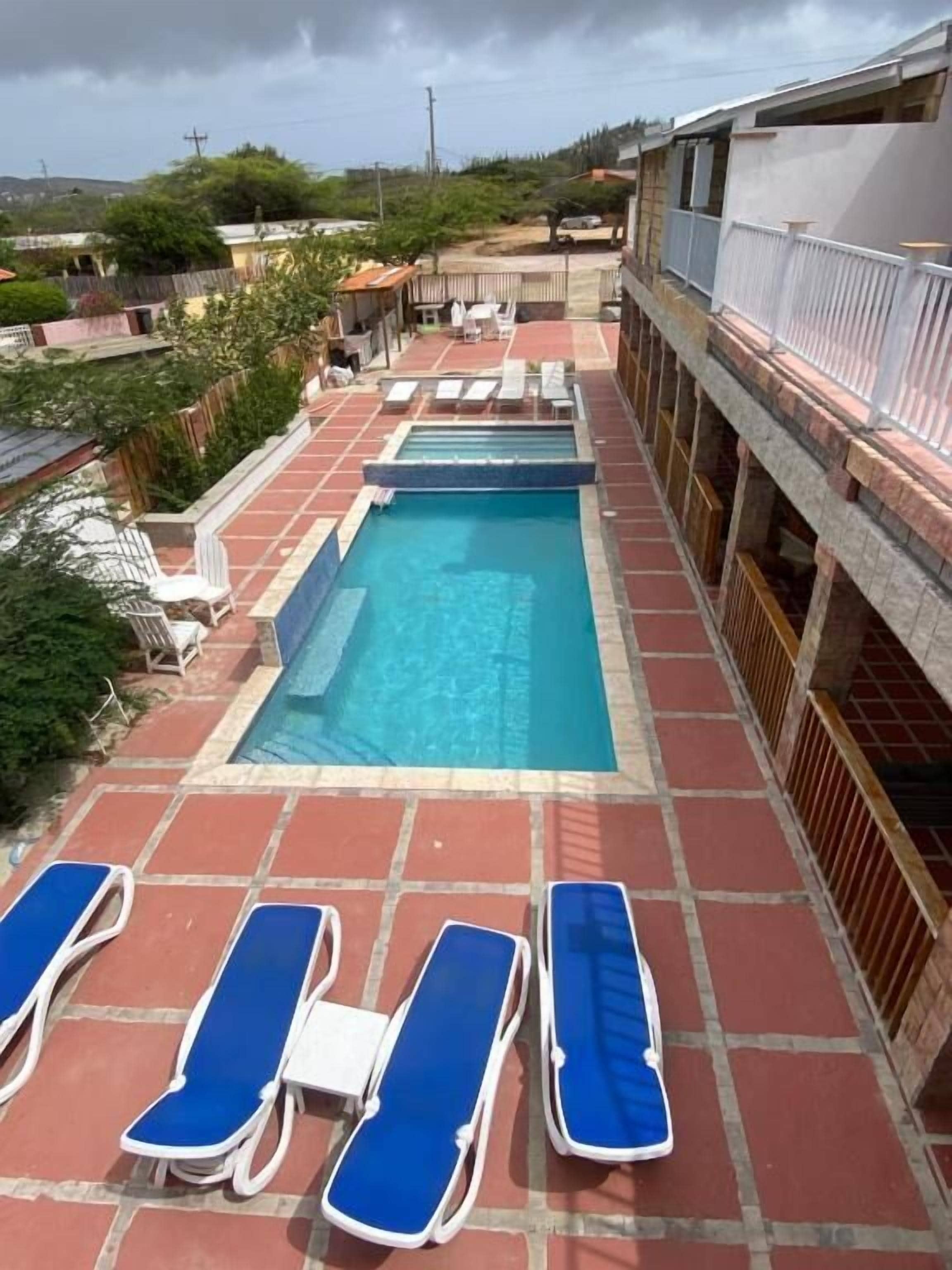 A rooftop swimming pool with blue lounge chairs and a tiled deck.