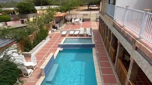 Una piscina en la azotea con sillones de descanso azules y una terraza con baldosas.