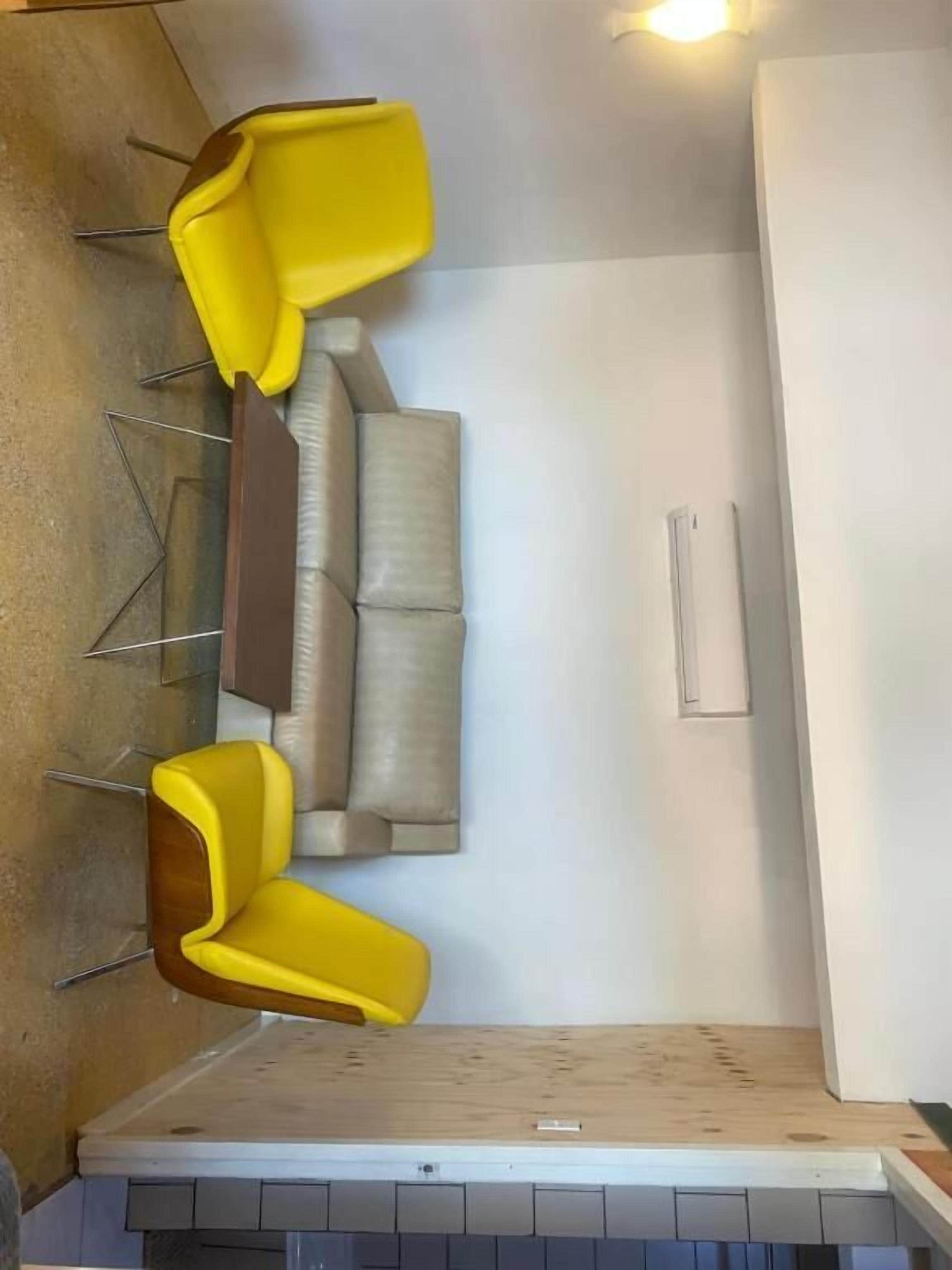 Ein Zimmer mit einer Couch, zwei gelben Stühlen, einem Holzboden und einer weißen Wand.