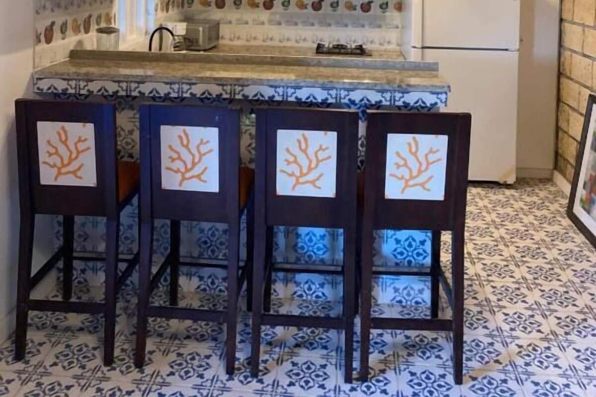 A kitchen with a wooden ceiling, white cabinets, a tiled backsplash, and a bar area with chairs.