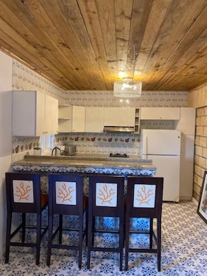 A kitchen with a wooden ceiling, white cabinets, a tiled backsplash, and a bar area with chairs.