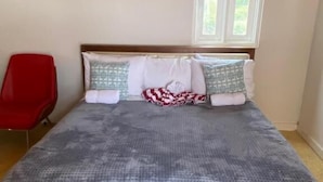 Una cama con una colcha estampada, dos almohadas, un cabecero de madera y una ventana arriba.