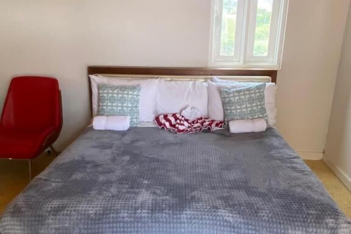 A bed with a patterned bedspread, two pillows, a wooden headboard, and a window above.