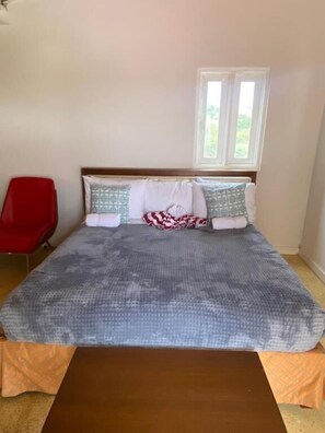 A bed with a patterned bedspread, two pillows, a wooden headboard, and a window above.