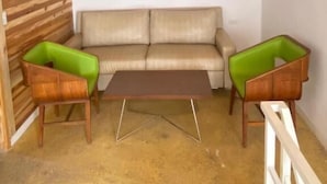 Quarto com teto de madeira, sofá bege, duas poltronas verdes e uma mesa de centro de madeira.