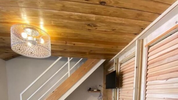 Una habitación con techo de madera, una escalera, un televisor montado en la pared y un piso con diseño.