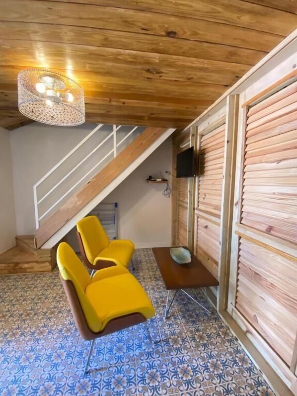 A room with a wooden ceiling, a staircase, a TV mounted on the wall, and a patterned floor.