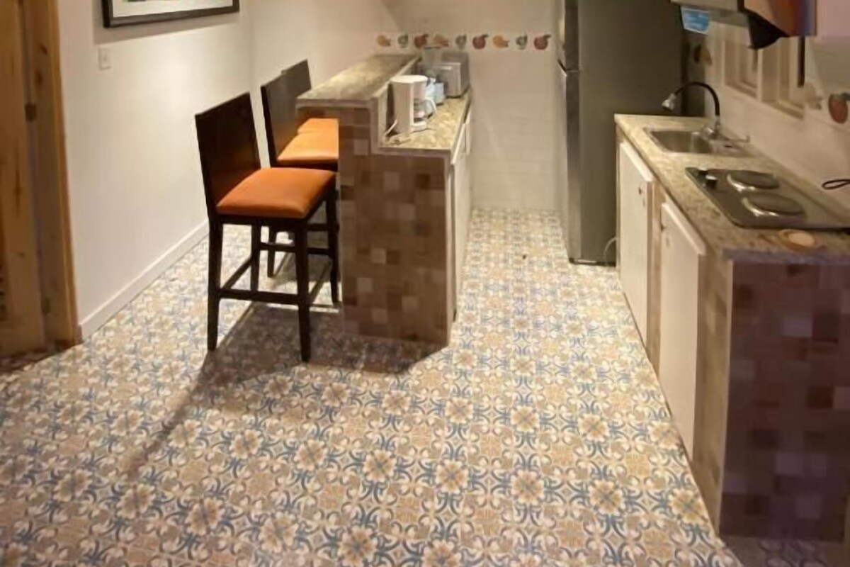 A compact kitchen with a wooden ceiling, a tiled floor, and basic amenities including a sink, stove, and a small dining area with chairs.