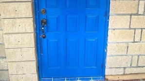 Una puerta azul con manija de metal y cerradura, ubicada en un muro de ladrillo.