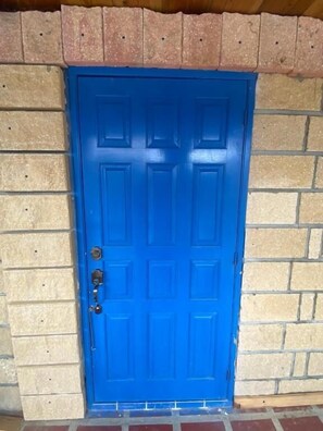 A blue door with a metal handle and a keyhole, set in a brick wall.