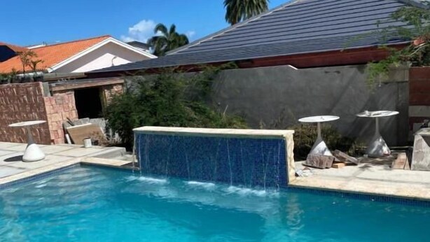 Piscina com cascata, rodeada por um terraço com mobiliário de exterior.