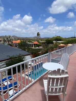 A balcony with a pool, white chairs, and a table. - Arco Iris Casa de Campo  (Santa Cruz)