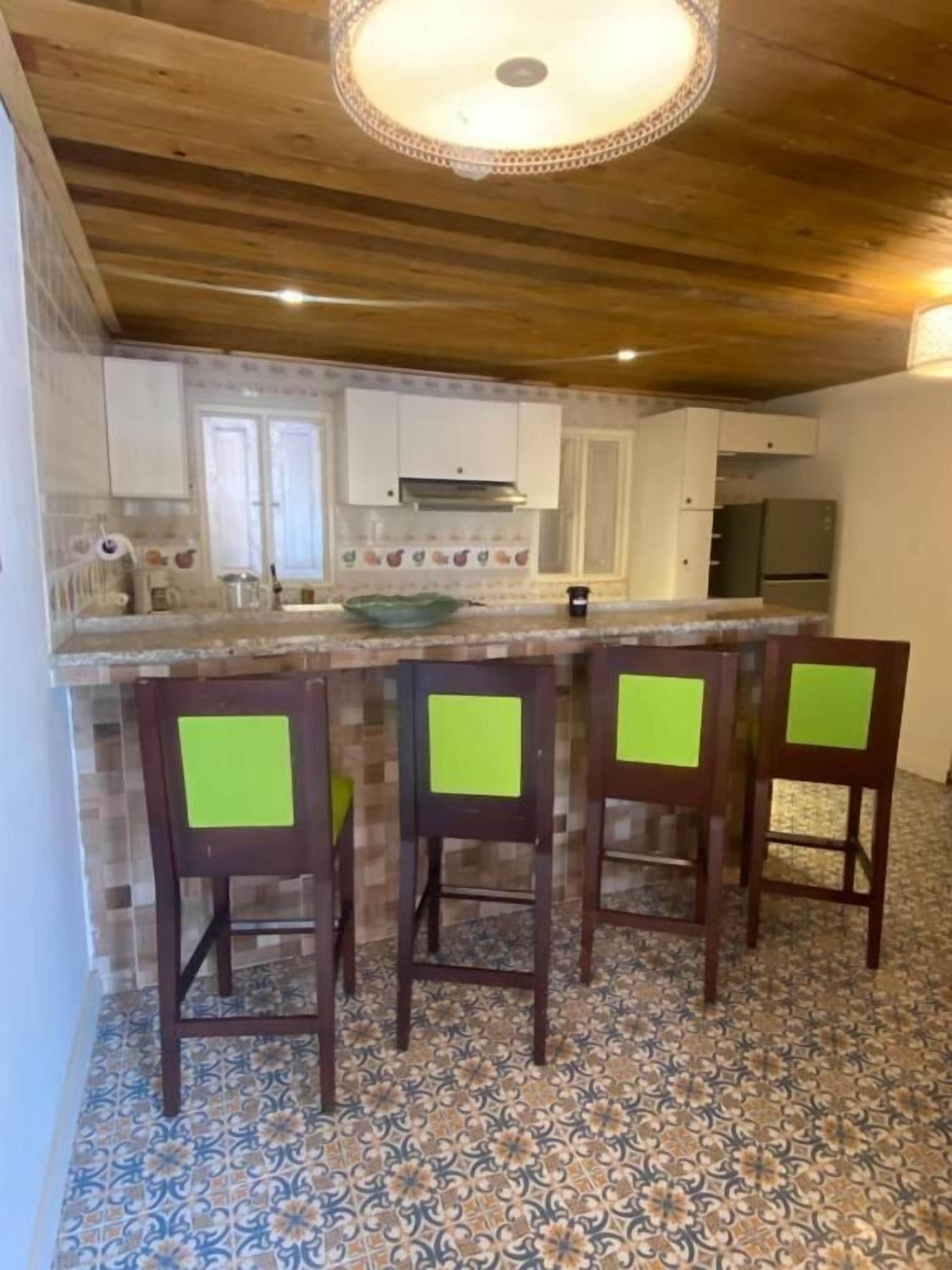Une cuisine avec un plafond en bois, un sol carrelé et un coin bar avec des chaises.