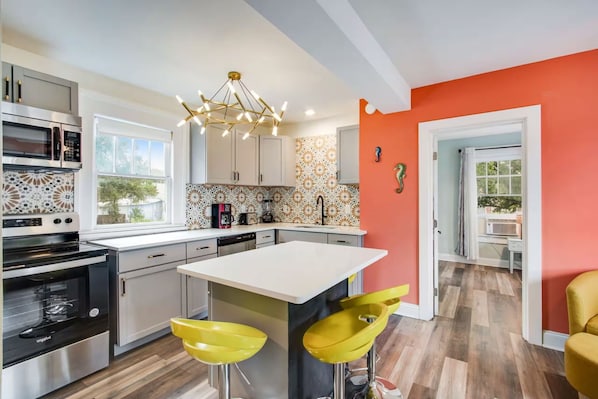 A modern kitchen with a central island, stainless steel appliances, and yellow bar stools. - Cozy Pensacola Escape - Close to Downtown & Beach (Pensacola)