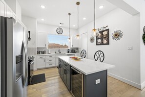 Uma cozinha moderna com armários brancos, uma ilha grande, iluminação pendente e arte decorativa na parede.