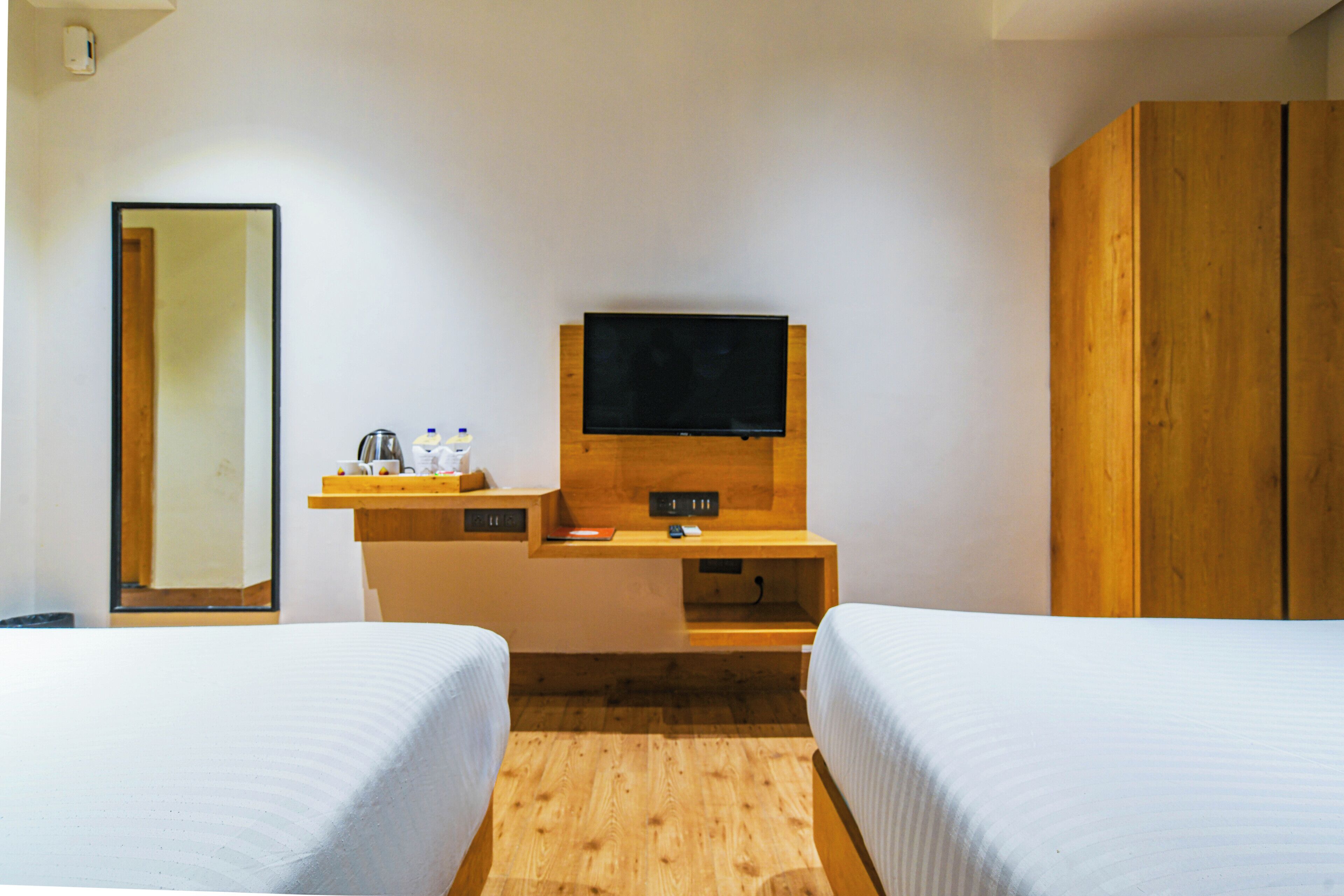 A hotel room with two beds, a TV, a wooden desk, and a wardrobe.