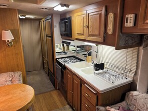 A compact kitchen with wooden cabinets, a microwave, a stove, and a sink.