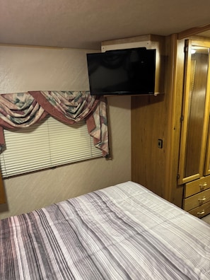 A bedroom with a bed, a television mounted above a window, and wooden cabinetry.