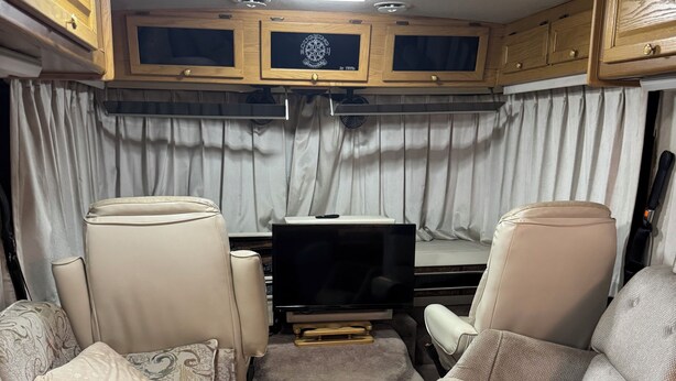 Ein kompaktes Wohnmobil-Interieur mit zwei beigen Ledersofas, einem Flachbildfernseher und Holzschränken.