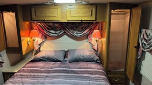 Ein Schlafzimmer mit einem Bett, zwei Nachttischlampen, einem Fenster mit Vorhängen und Holzschränken über dem Bett.