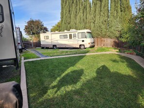 A recreational vehicle parked in a yard with a wooden fence and a grassy area.