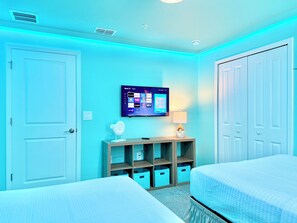 Une chambre d’hôtel avec deux lits, un téléviseur fixé au mur et une petite table avec une lampe.