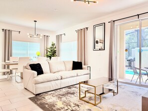 A modern living room with a sofa, coffee table, and dining area. - 5-bedroom townhome with Club Access, PVT Pool, BBQ Grill just 15 min from Disney (Kissimmee)