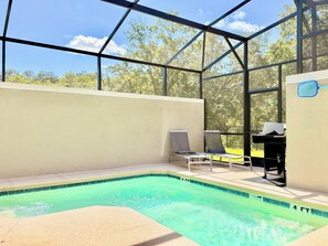 A pool area with a clear view of trees outside, a covered seating area with chairs, and a pool ladder. - 5-bedroom townhome with Club Access, PVT Pool, BBQ Grill just 15 min from Disney (Kissimmee)